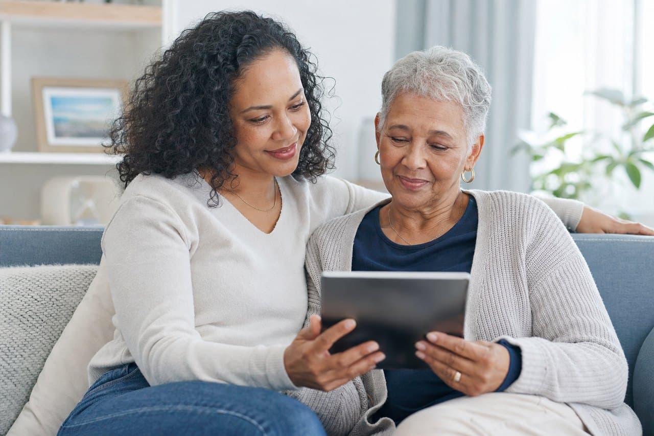 An adult daughter and her mother looking at a tablet together on a sofa
